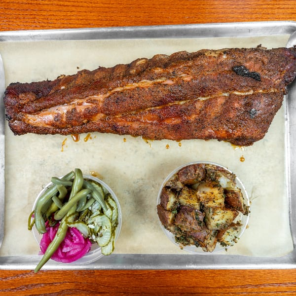 Smoked barbecue ribs served on a tray with seasoned potatoes and pickled green beans.