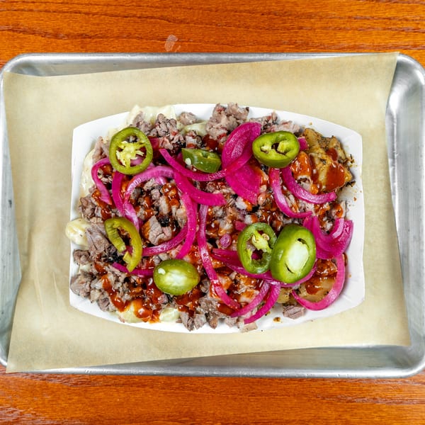 Loaded fries topped with chopped meat, melted cheese, hot sauce, pickled onions, and sliced jalapeños in a paper tray.