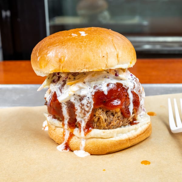 Saucy pulled-meat sandwich on a toasted bun with creamy slaw, served on parchment with a fork.