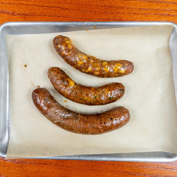 Three browned, cheese-topped sausages arranged on parchment paper in a metal baking tray.