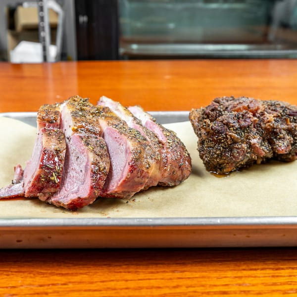 Sliced herb-crusted roast beef and a whole pepper-crusted roast sit on parchment atop a metal tray.