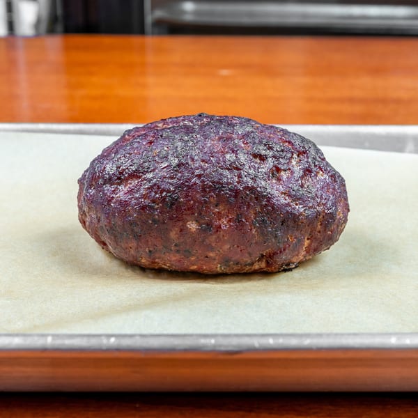 A large charred burger patty rests on parchment paper atop a metal tray in a restaurant kitchen.